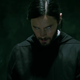 Morbius, wearing a black smock in a darkened room, looks down while his eyes roll inside his head.
